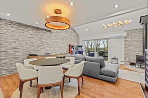 A modern living room with a dining area, grey sofa, wooden table, and a fireplace.