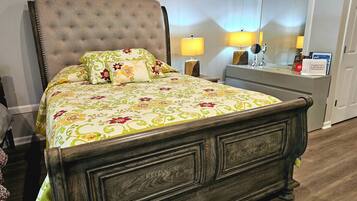 Un lit recouvert d’une couvre-lit à motifs floraux, une table de chevet avec des lampes et une commode avec un miroir.