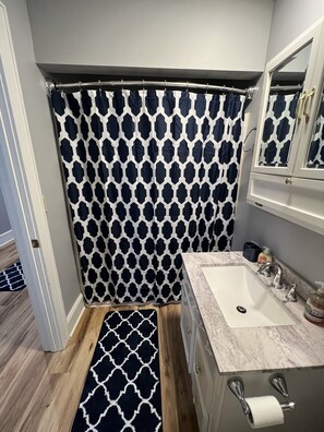 Un baño con cortina de ducha, lavamanos, espejo y suelo de madera.