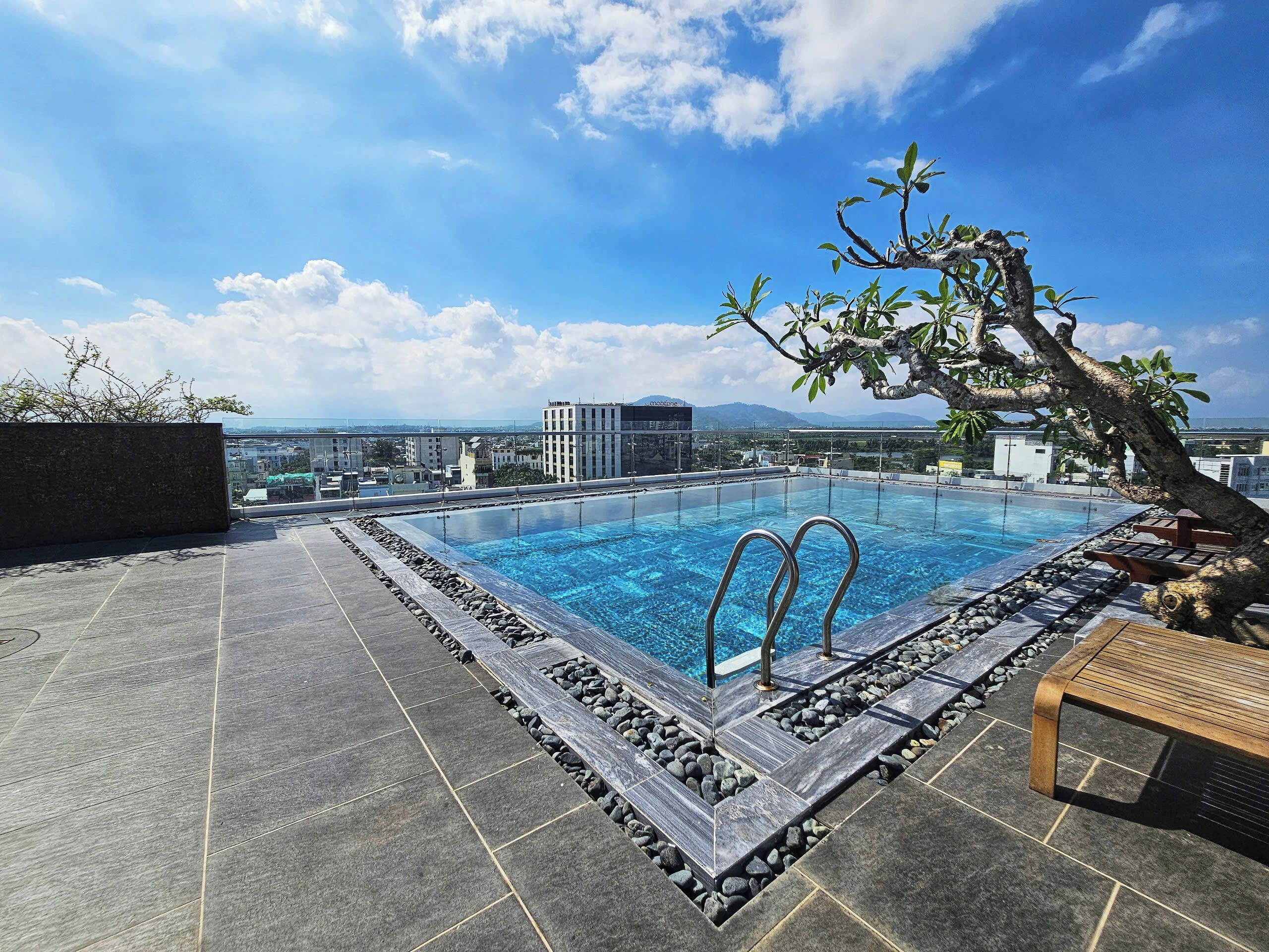 A rooftop infinity pool with a clear view of the city skyline and mountains in the distance.