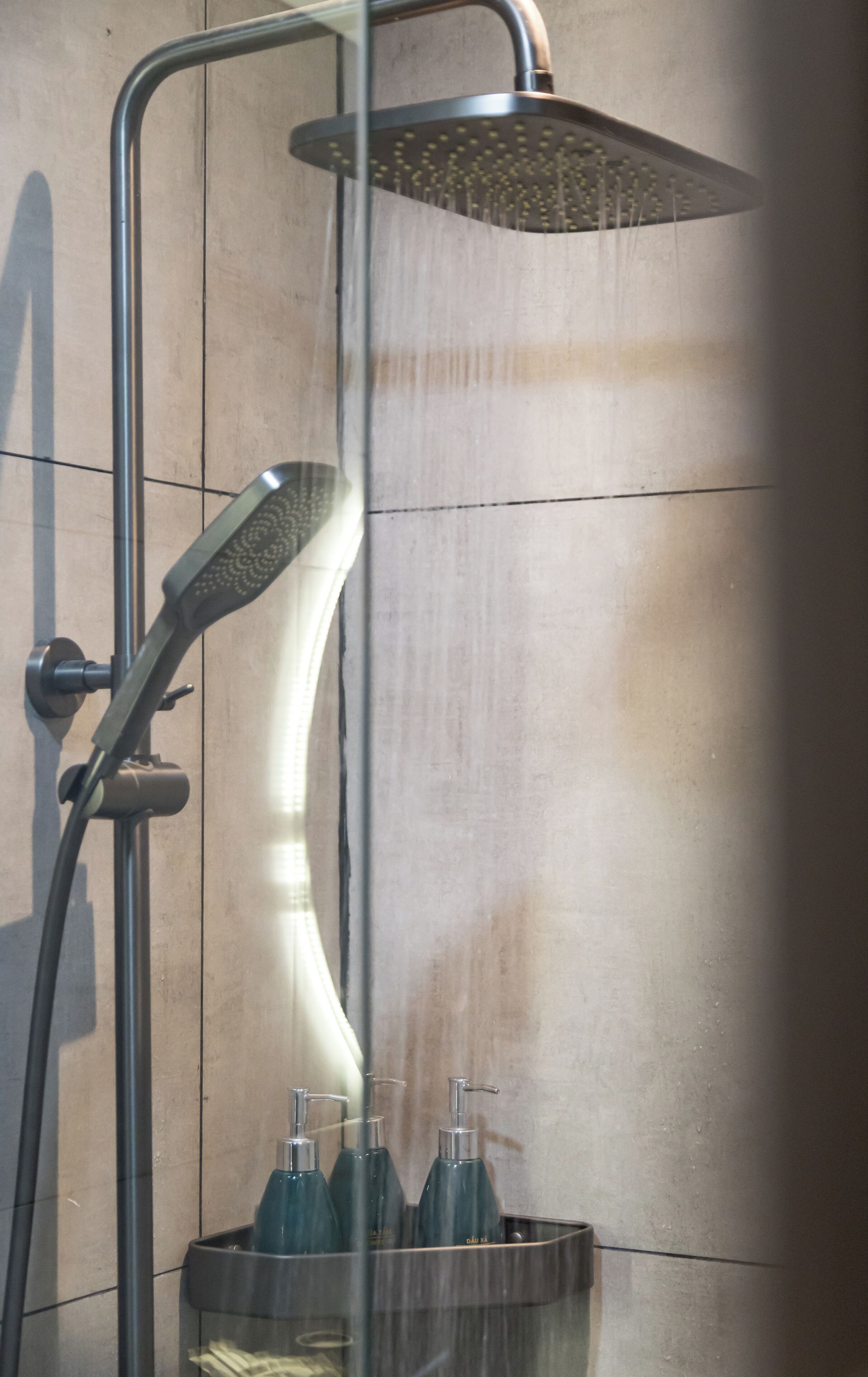 A shower with a rain head, a handheld showerhead, and a soap dispenser.