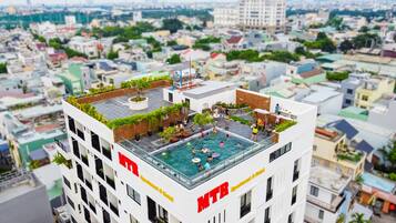 A modern hotel with a rooftop pool, surrounded by greenery and a cityscape view.