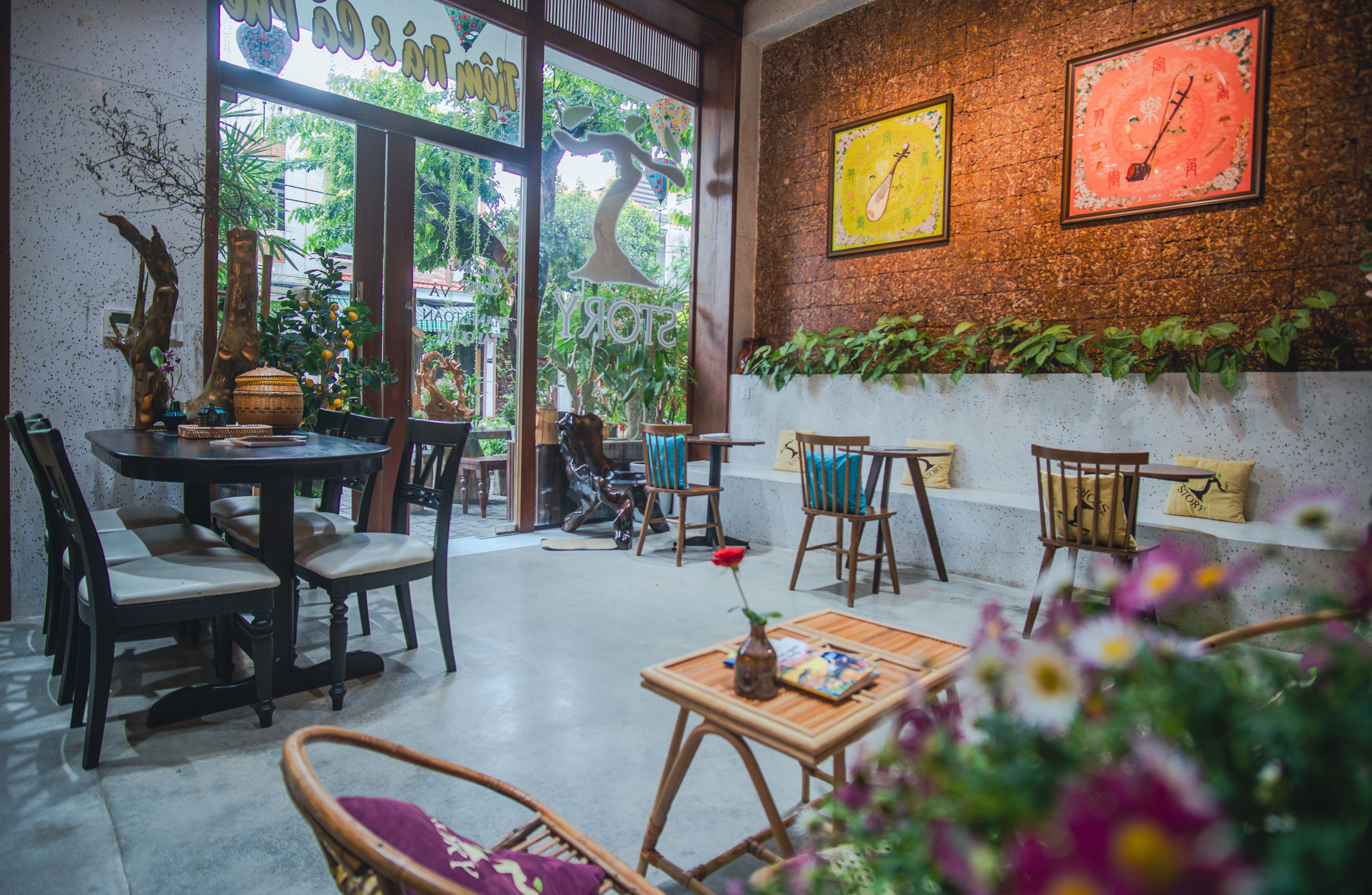 A cozy cafe with a rustic brick wall, wooden furniture, and a view of greenery outside.