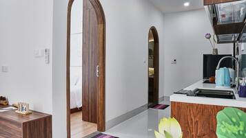 A modern hotel room with a wooden door, a small desk, a bed, a bathroom, and a kitchenette.