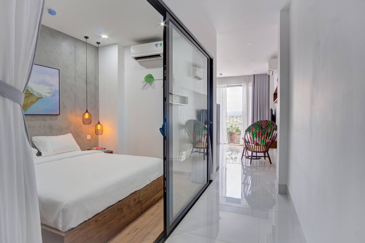A modern bedroom with a glass door leading to a balcony, a bed with a wooden headboard, and a painting on the wall.