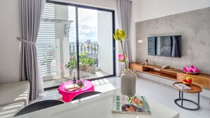 A modern living room with a large window, a flat-screen TV, a dining table, and a sofa. - LAM Apartment & Hotel Danang (Da Nang)