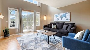 A living room with a sofa, a coffee table, and a blue armchair. There is a world map on the wall and a plant on the floor. - Cozy Condo | Epic Mountain Views | Parking Garage | Central | Air Conditioning (Canmore)