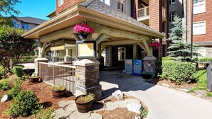 A hotel entrance with a covered porch, stone pillars, and potted plants. - Cozy Condo | Epic Mountain Views | Parking Garage | Central | Air Conditioning (Canmore)