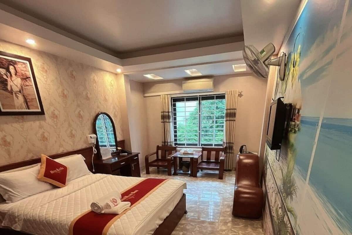 A hotel room with a bed, a desk, a chair, a TV, and a mural on the wall.