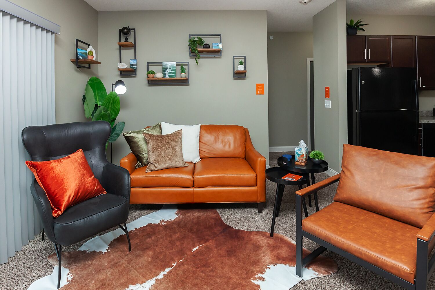 A living room with a sofa, two armchairs, a cowhide rug, and wall-mounted shelves with plants and pictures.