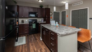 Une cuisine moderne avec des meubles de couleur bois foncé, un réfrigérateur noir, un four encastré et un îlot central doté d’un comptoir en granit et de tabourets de bar.