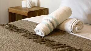 A neatly made bed with rolled towels, a small wooden nightstand with a plant and a roll of toilet paper. - Malayah Hostel (General Luna)