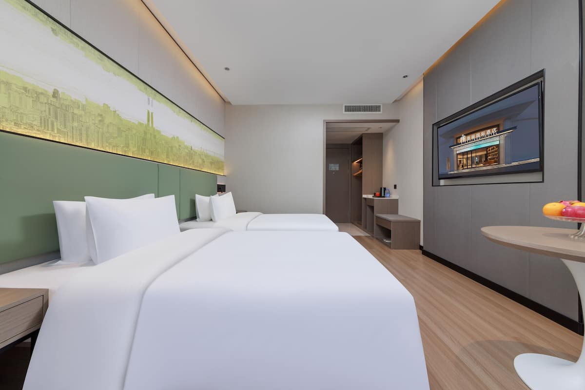 A hotel room with a cityscape mural, a bed, a desk, and a small table with fruit.