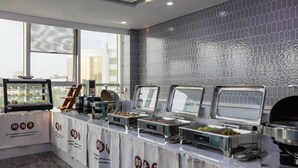 Un'area buffet con diverse postazioni coperte di cibo, un'ampia vetrata e uno schienale piastrellato.