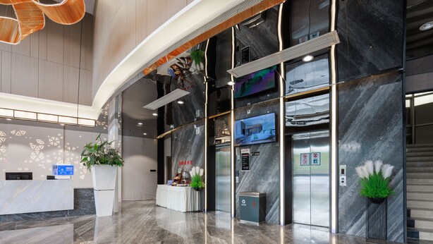 Una hall moderna con una reception, un pannello informativo digitale e un’area accoglienza con una pianta.