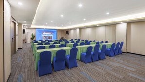 Una sala conferenze con file di tavoli e sedie, uno schermo di proiezione e un pavimento con tappeto.