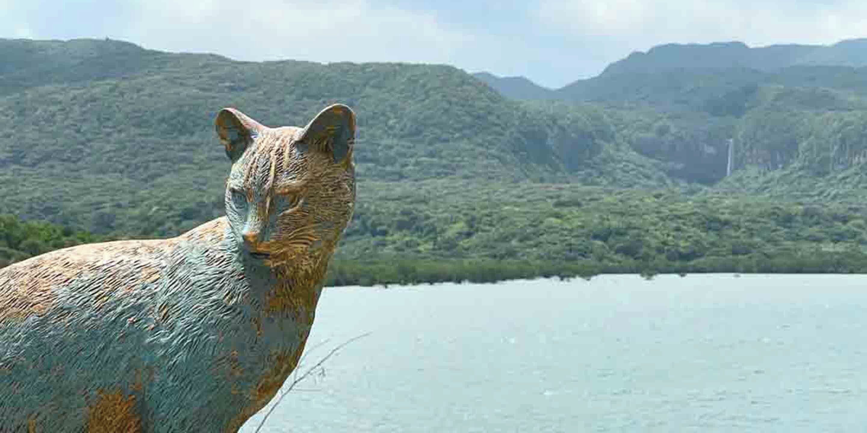 A sculpture of a cat-like animal with a mountainous landscape in the background.