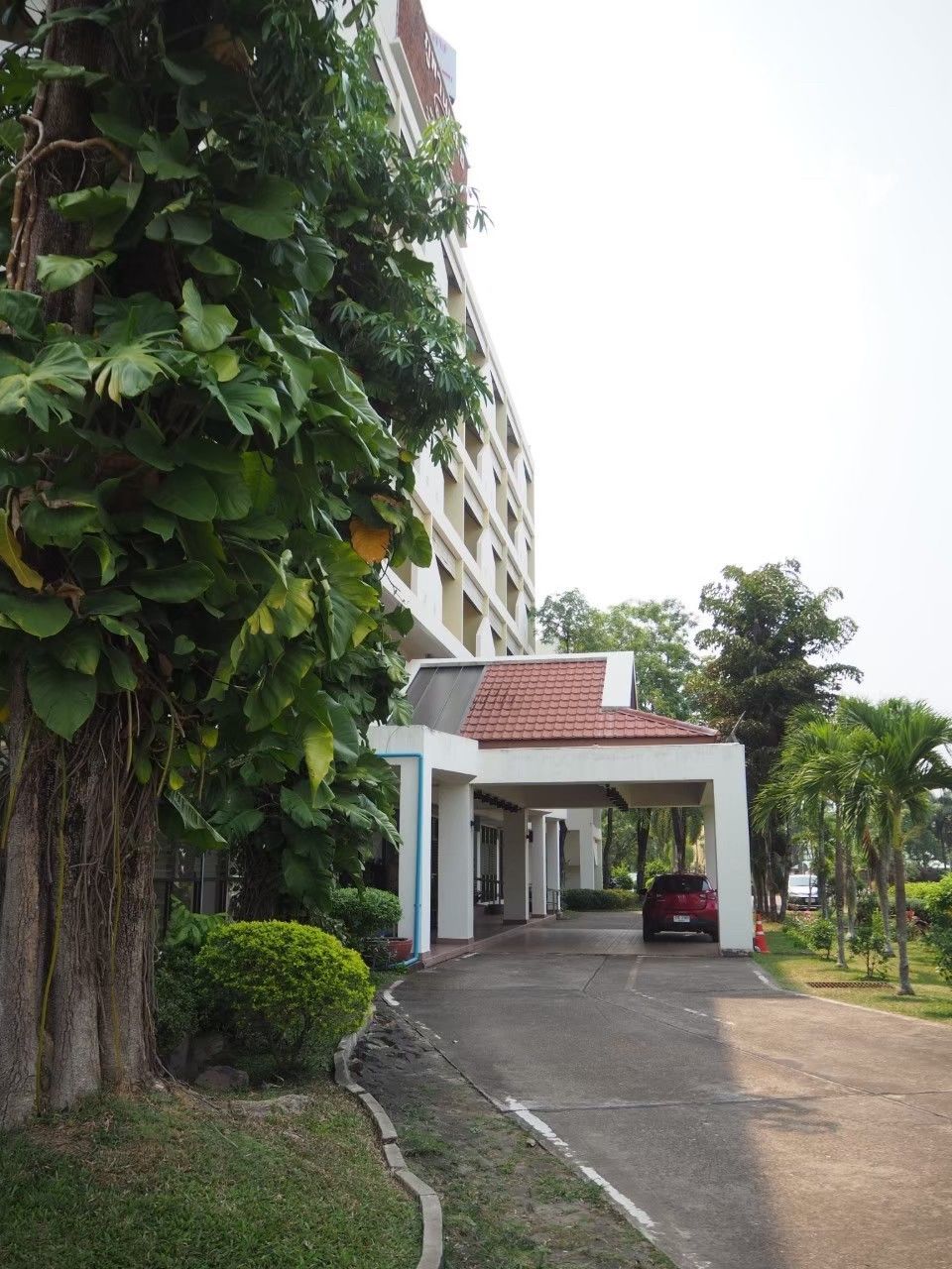 A building with a covered entrance, a red car parked in front, and a well-maintained garden area.