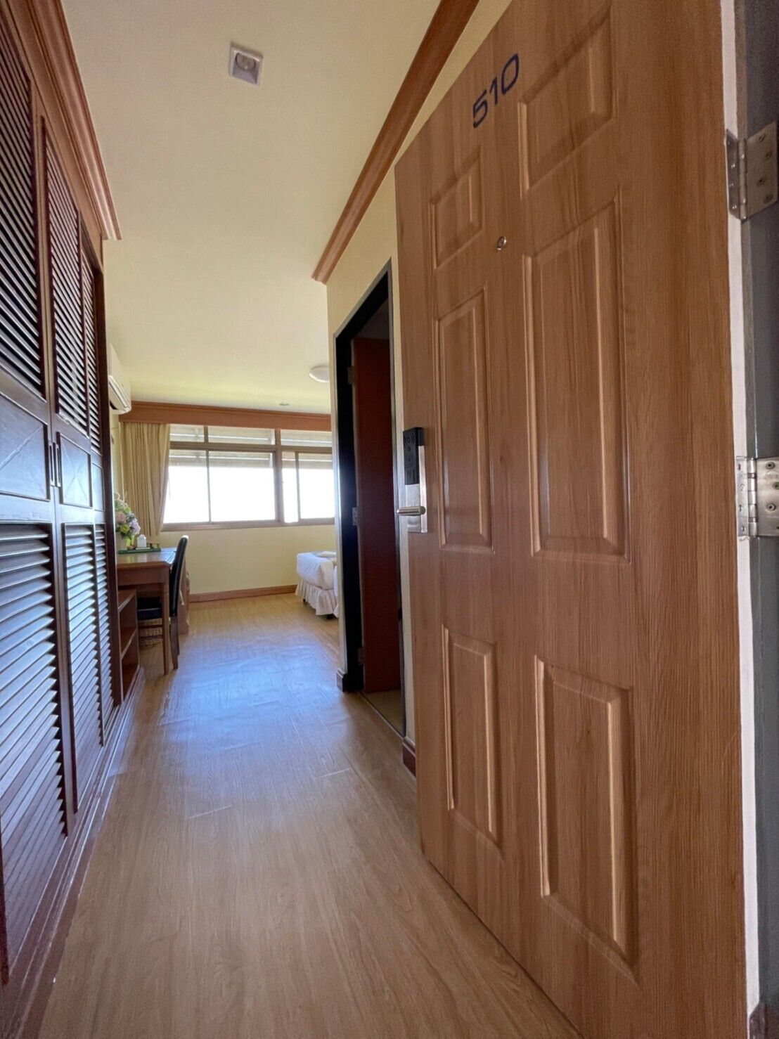 A hallway with a wooden door marked "510", a window with blinds, and a bed in the background.