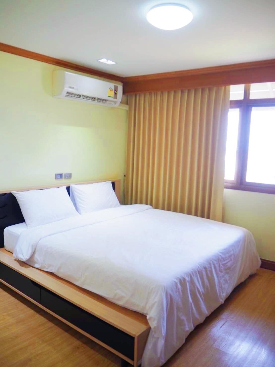 Habitación de hotel con una cama individual, suelo de madera, aire acondicionado instalado en el techo y una ventana con cortinas.