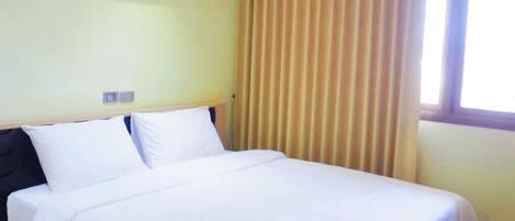 Habitación de hotel con una cama individual, suelo de madera, aire acondicionado instalado en el techo y una ventana con cortinas.