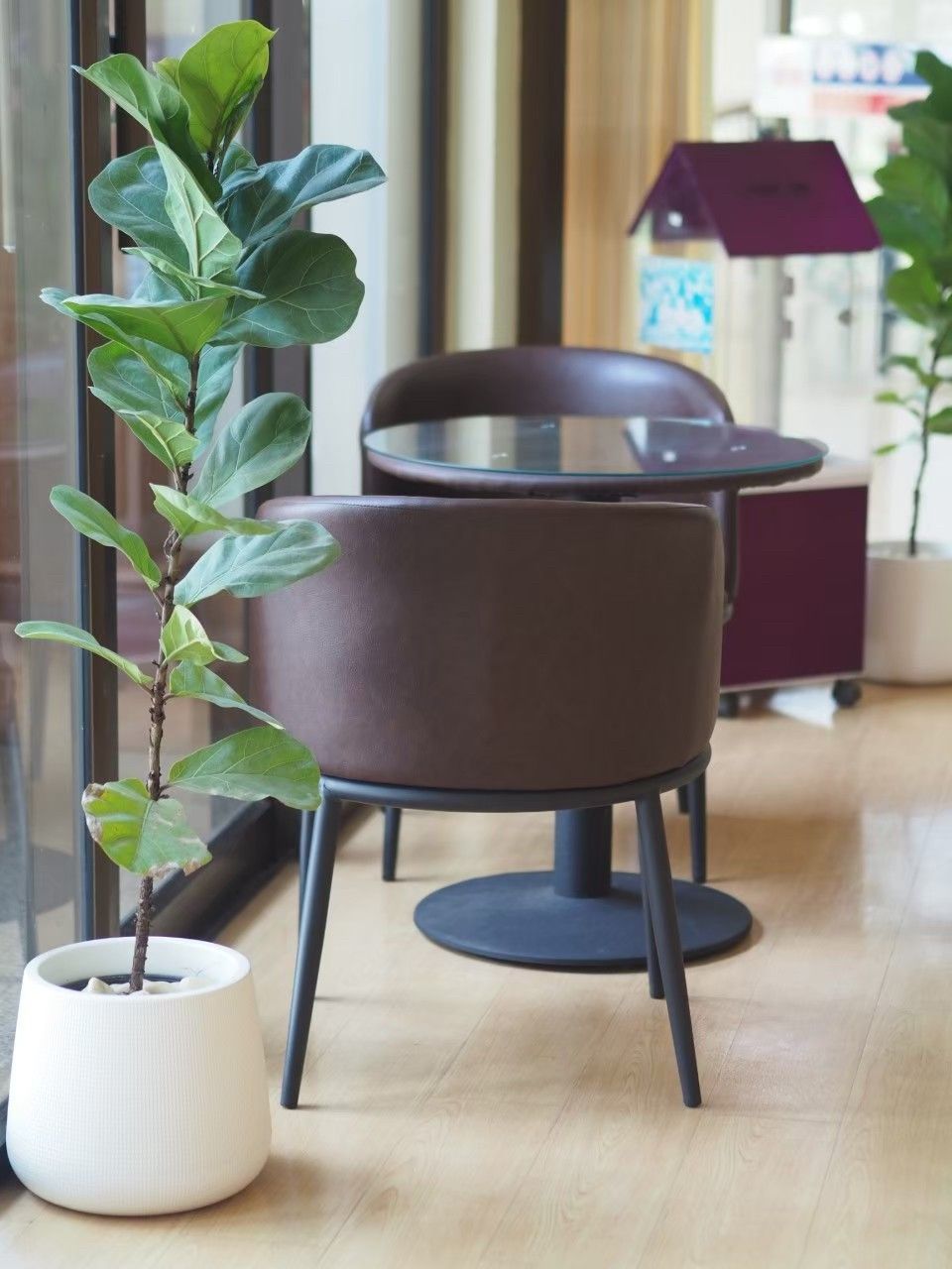 A modern indoor setting with a round table and a chair, a potted plant, and a wooden floor.