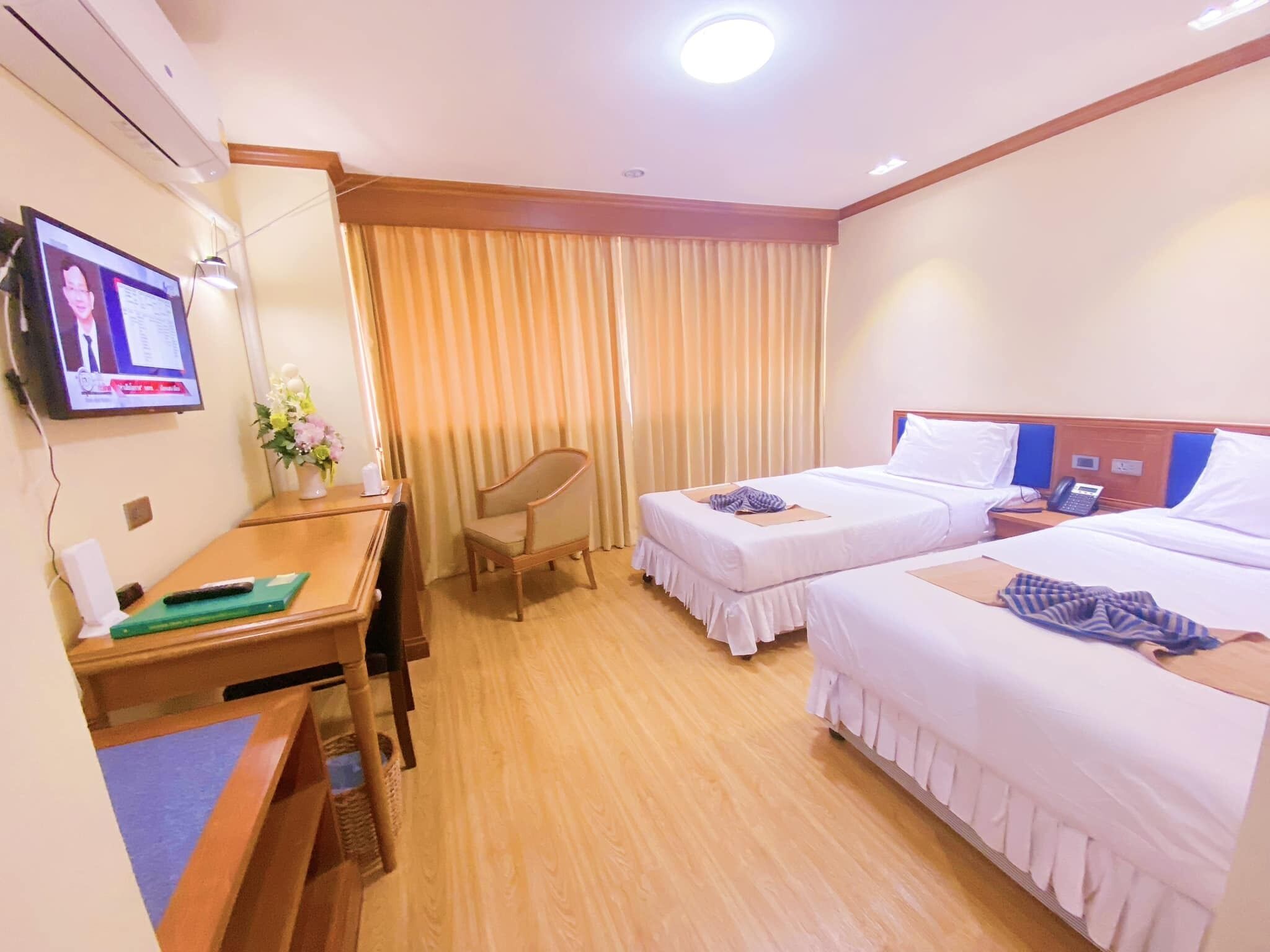 A hotel room with two beds, a desk, a chair, a TV, and a window with curtains.