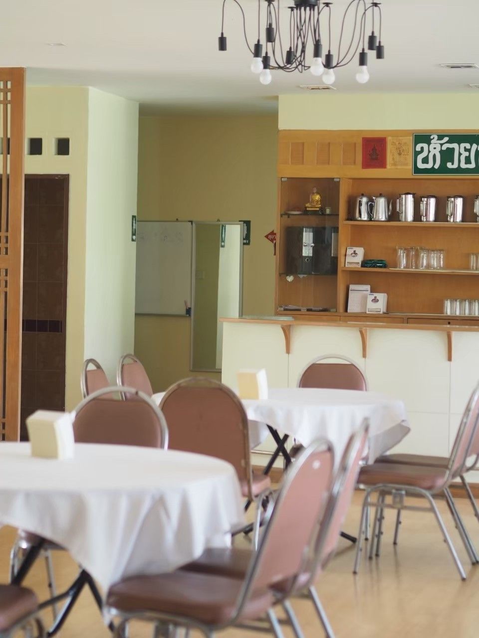A dining area with tables and chairs, a kitchen area with shelves, and a sign with text.
