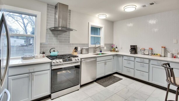 A modern kitchen with white cabinets, stainless steel appliances, a window, and a built-in stove. - Central Austin 6 Bedroom Gem (Austin)