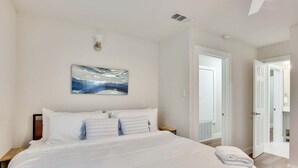 A large bed with white linens, a painting of a wave on the wall, and a view of a balcony through an open door. - Central Austin 6 Bedroom Gem (Austin)