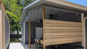 A covered patio area with a table and chairs, a ceiling fan, and two trash bins. - Central Austin 6 Bedroom Gem (Austin)