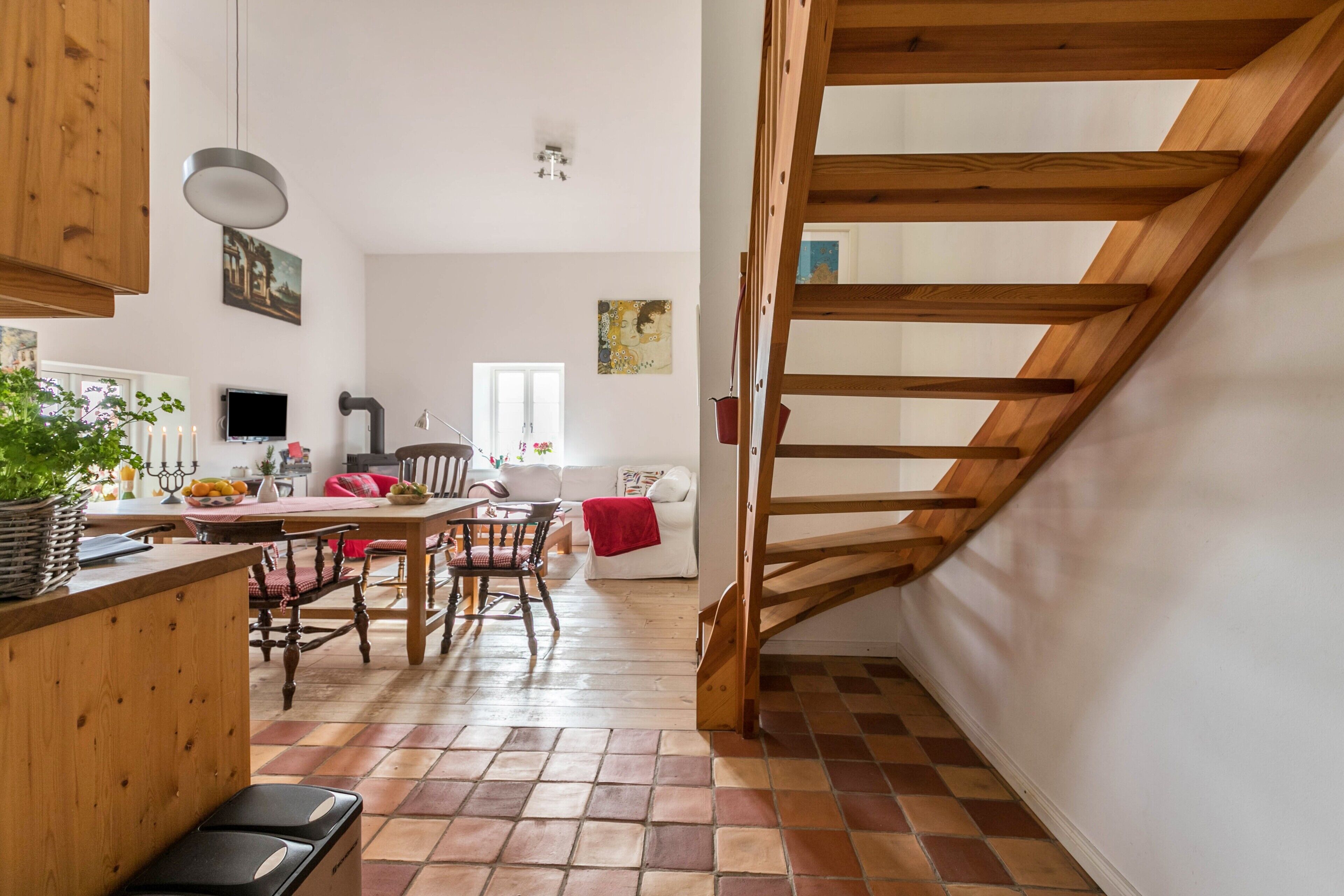 Eine Küche mit Holzausstattung, einem Esstisch und Stühlen, einer Treppe und einem Wohnbereich mit Sofa und Fernseher.