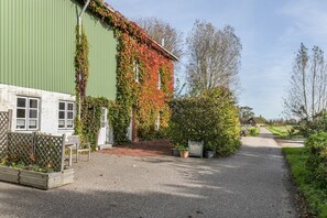 A building with a green exterior, a wooden fence, and a gravel path leading to a house. - Apartment 'Mühlenhof Ferienwohnung 3a' with Wi-Fi (Hillgroven)