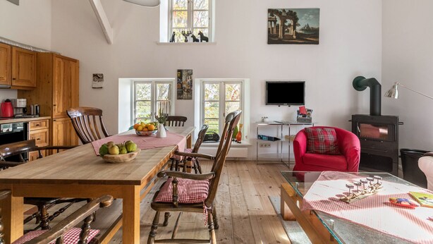 Ein geräumiger Wohnbereich mit einem Holzessttisch, Stühlen, einem roten Sessel, einem Kamin und einem Fernseher.