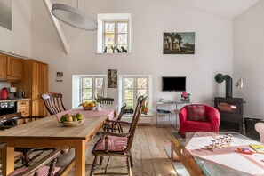 A spacious living area with a wooden dining table, chairs, a red armchair, a fireplace, and a television. - Apartment 'Mühlenhof Ferienwohnung 3a' with Wi-Fi (Hillgroven)