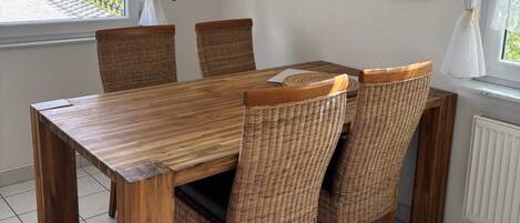 A dining area with a wooden table and wicker chairs, white curtains, and framed pictures on the wall.