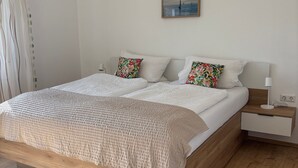 A modern bedroom with a wooden bed frame, white bedding, and a nightstand with a lamp. - Apartment 'Sonnenblume' with Private Terrace, Private Garden and Wi-Fi (Sipplingen)