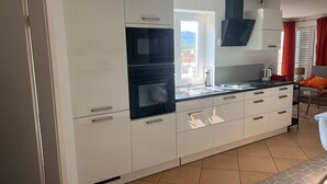 Une cuisine moderne avec des meubles blancs, un four encastré et une fenêtre donnant sur l’extérieur.