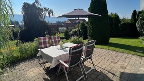 Une terrasse extérieure avec une table et des chaises, un grand parasol et une vue sur les maisons au loin.