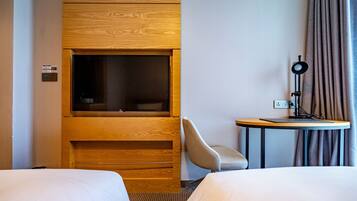 Une chambre d’hôtel avec deux lits, une télévision, un bureau avec une lampe et une chaise.