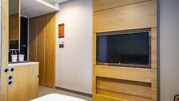 A modern hotel room with a wooden cabinet, a flat-screen TV mounted on the wall, and a small kitchenette area.