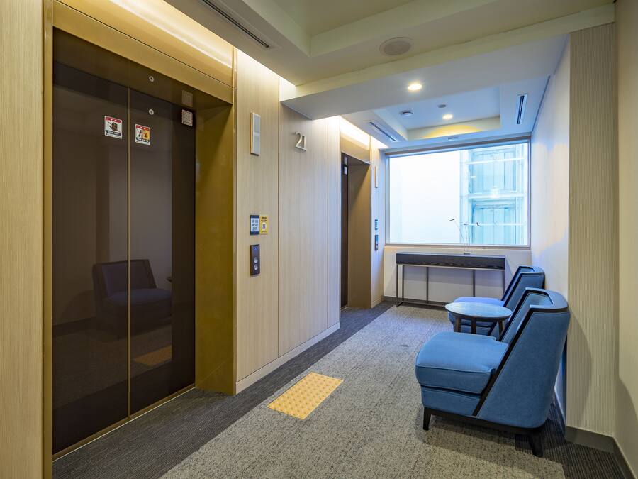 An elevator with a glass door, a carpeted floor, and a seating area with chairs and tables.