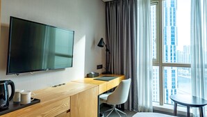 A hotel room with a large flat-screen TV, a wooden desk, a chair, a small table, and a view of the city through large windows. - Centum Business Hotel (Busan)