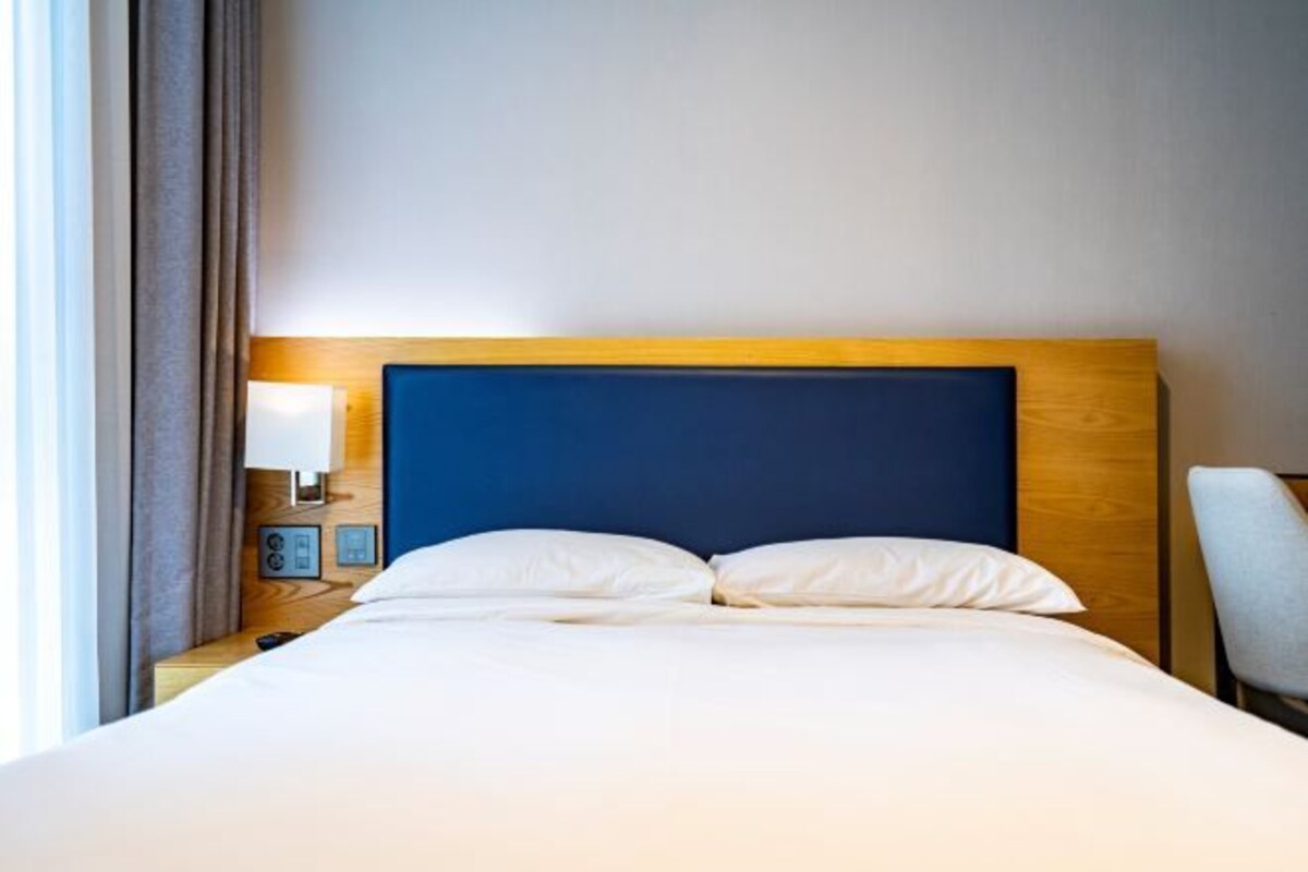 Una habitación de hotel con una cama, una mesita de noche, una lámpara y una silla.