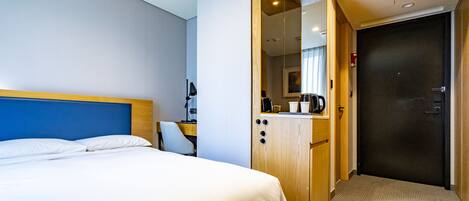 A hotel room with a bed, a desk with a computer, a mirror, and a door.