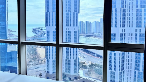 A view through a window of high-rise buildings, a bridge, and a body of water. - Centum Business Hotel (Busan)