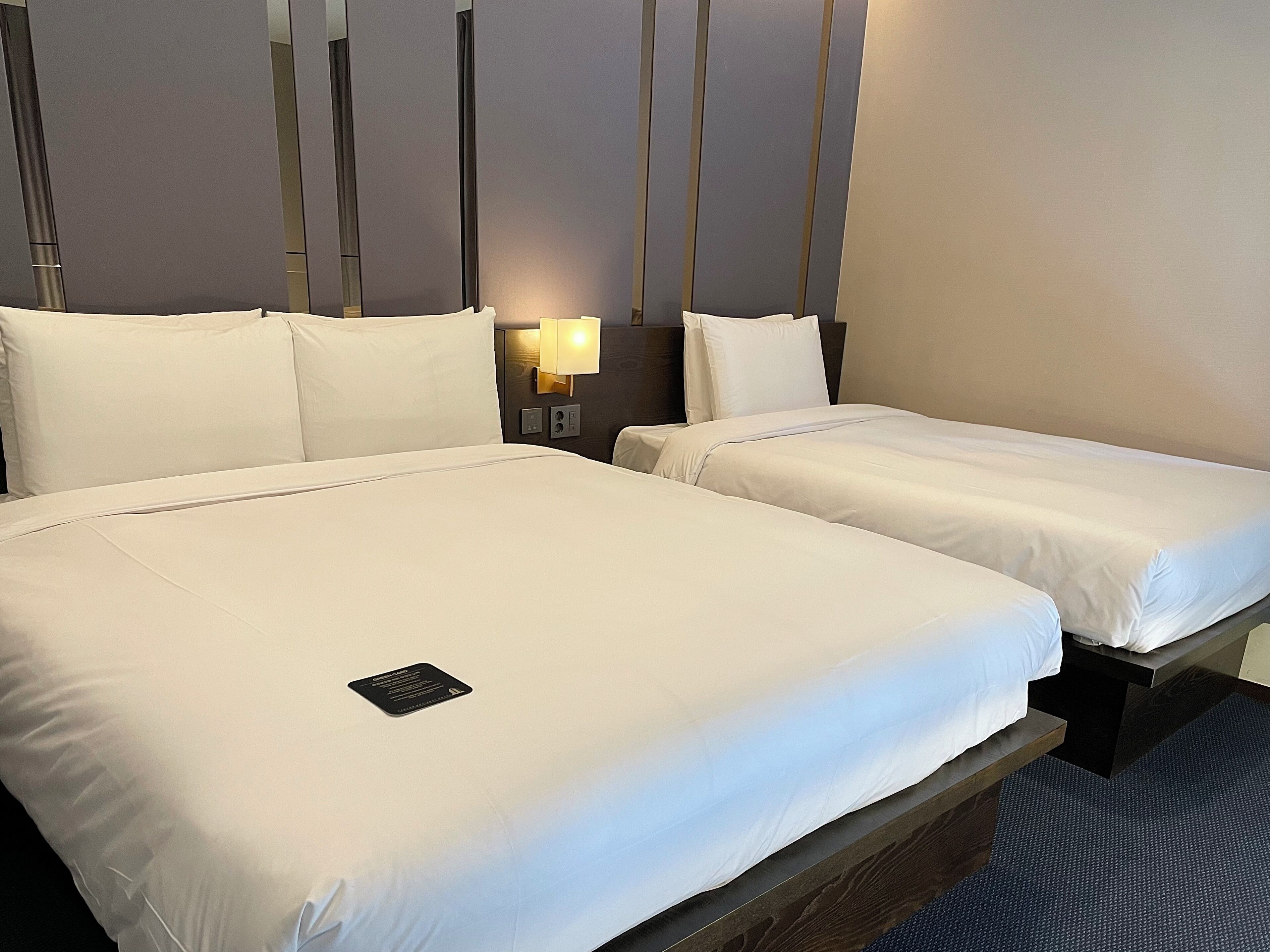 A hotel room with two single beds, a bedside table with a lamp, and a small bedside table with a phone.