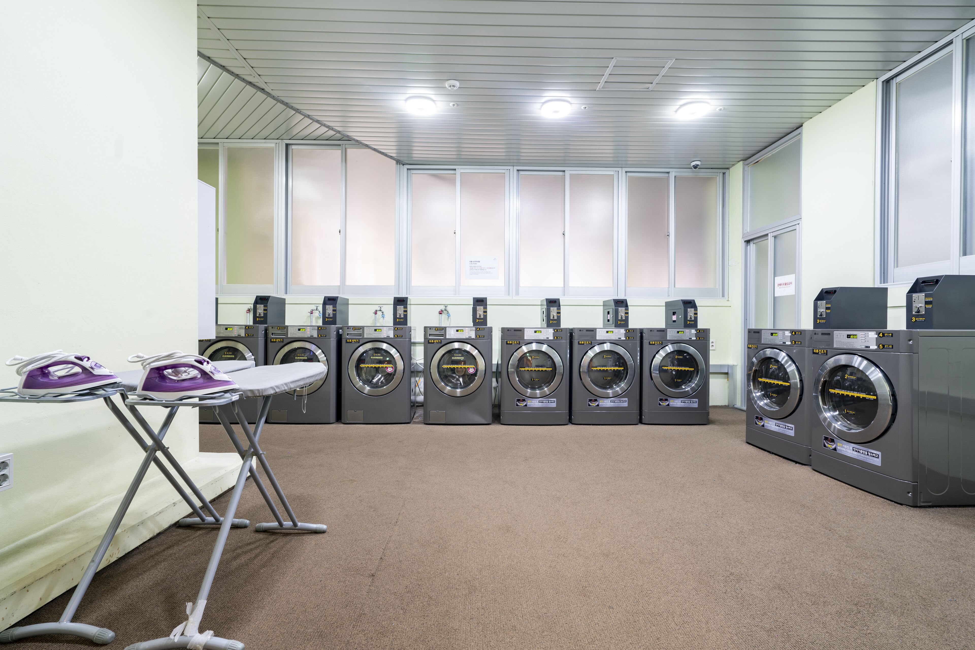 A laundry facility with multiple washing machines and ironing stations.