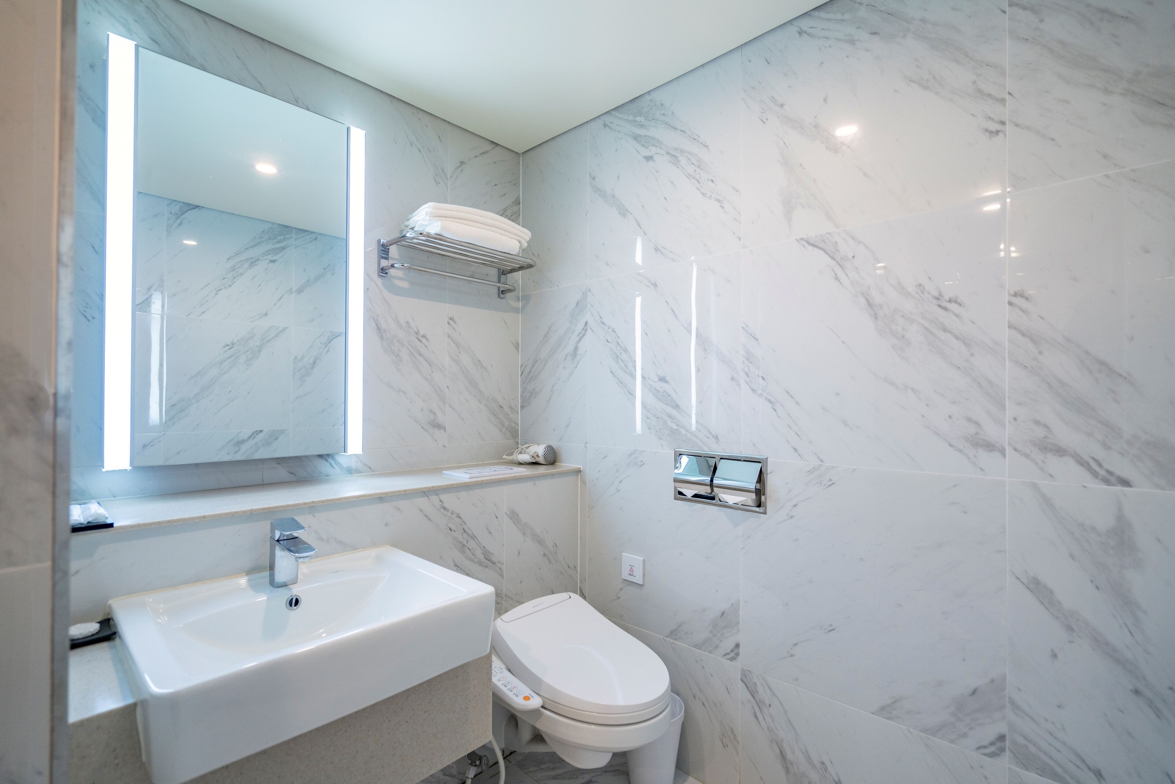 A modern bathroom with a marble wall, a white sink, a toilet, and a towel rack.