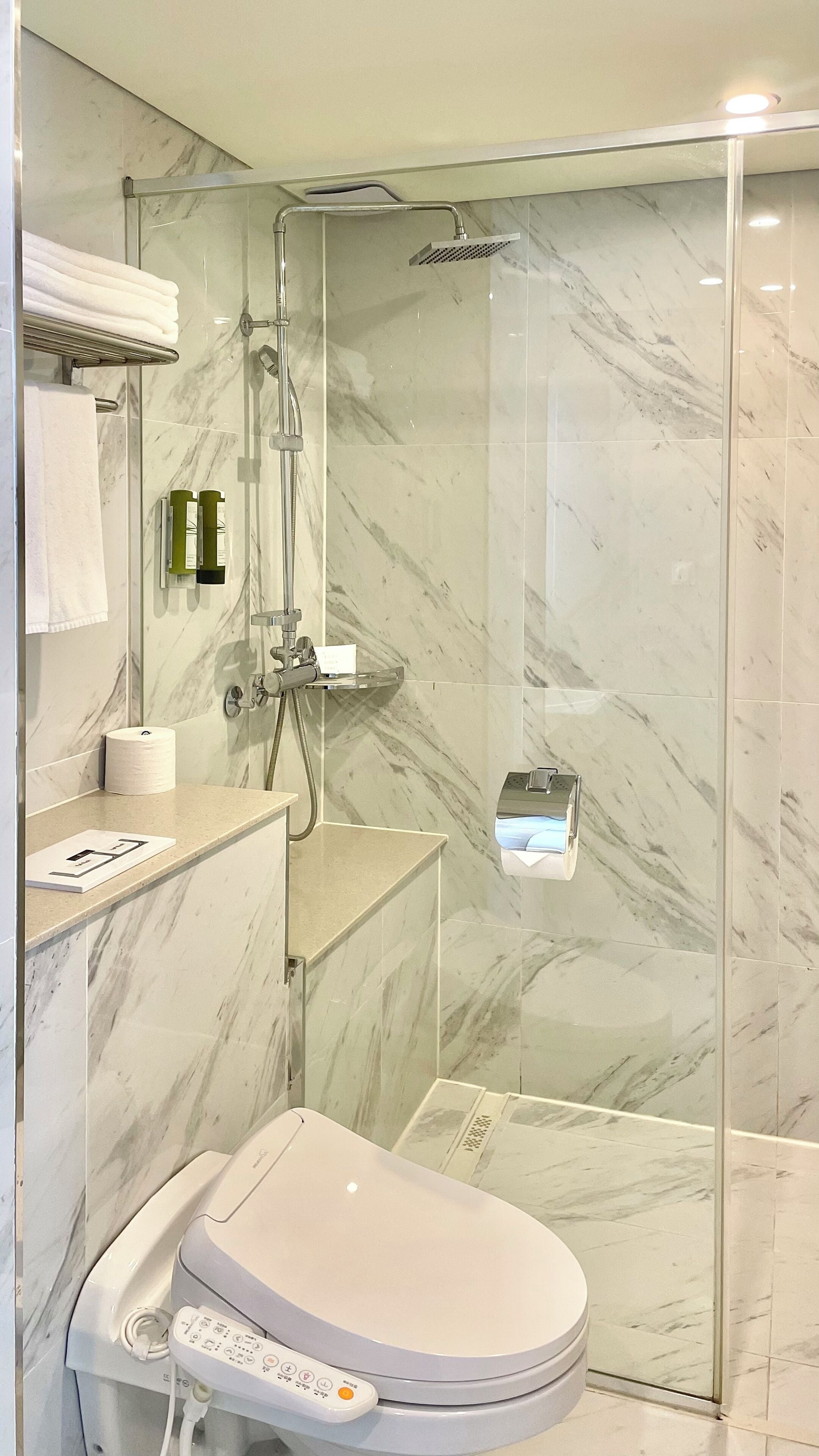 A modern bathroom with a glass-enclosed shower, a toilet with a control panel, and marble walls.